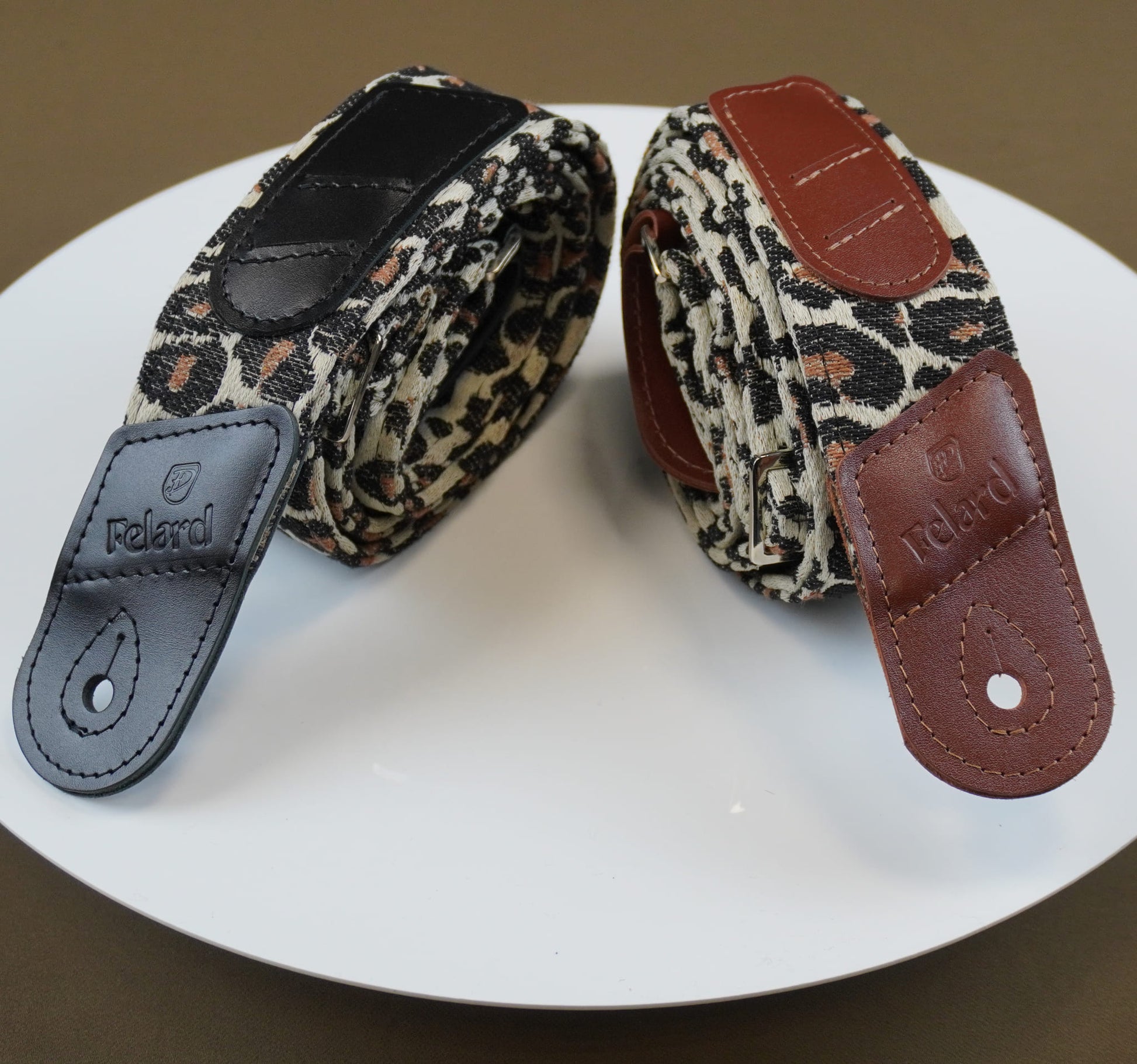 Felard guitar straps with leopard print fabric and leather accents, displayed on a white plate against a brown background.