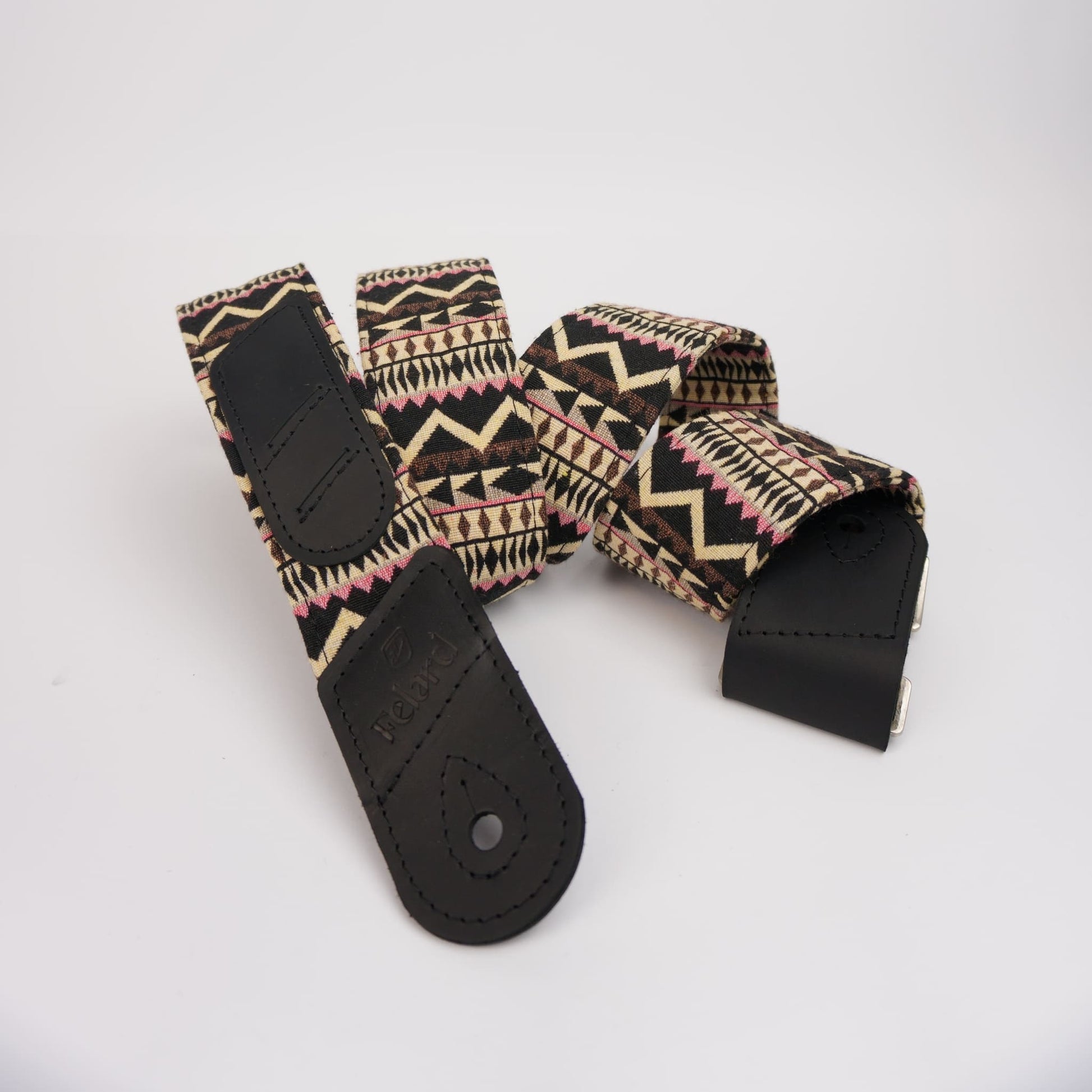 guitar strap with a black, beige, and pink geometric pattern, featuring black leather end caps and a metal snap button.