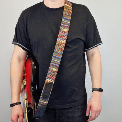 holding a red electric guitar and wearing a colorful patterned guitar strap with a geometric design.