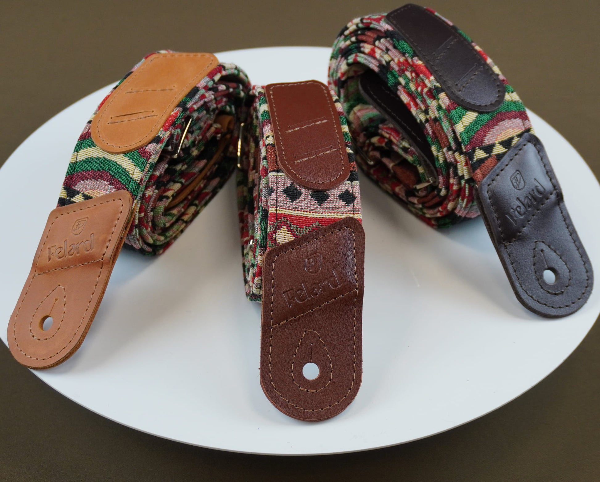 Three guitar straps with leather ends displayed on a white plate. The center strap is shown flat with its brown leather end facing forward, revealing the brand name 'feard' and a shield logo.