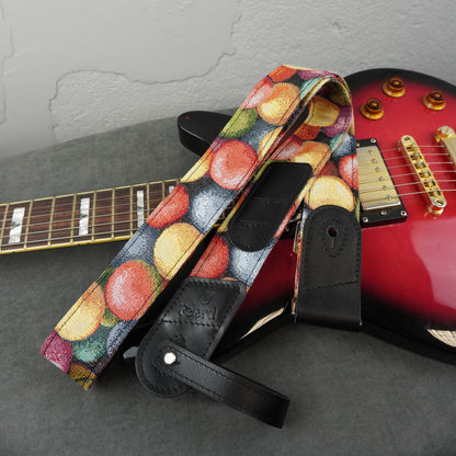 Guitar strap with a colorful macaron pattern and black leather accents, draped over a red electric guitar on a gray surface.