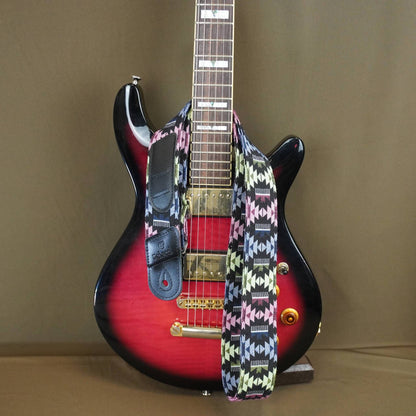 colorful geometric patterned guitar strap draped over the body, set against a plain brown backdrop.
