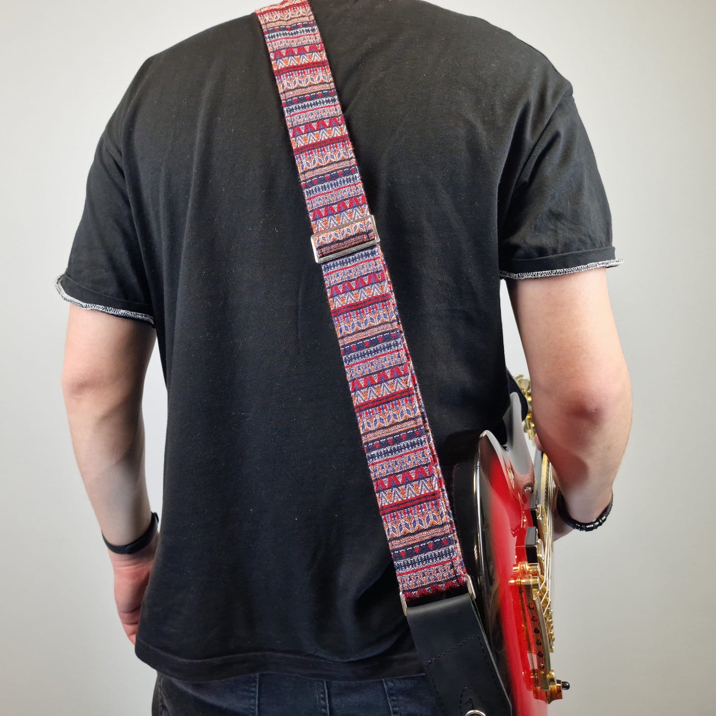 showcasing a patterned guitar strap with red, blue, and white geometric designs.