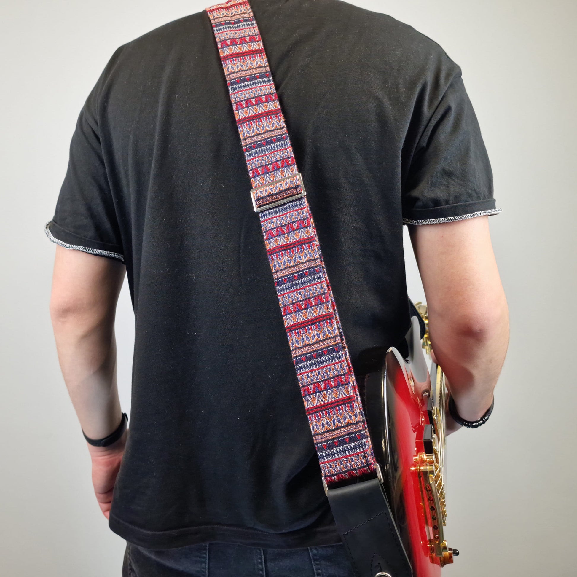 showcasing a patterned guitar strap with red, blue, and white geometric designs.