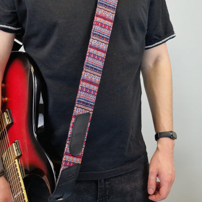 showcasing a patterned guitar strap with a geometric design in red, blue, and white, and a black leather patch.