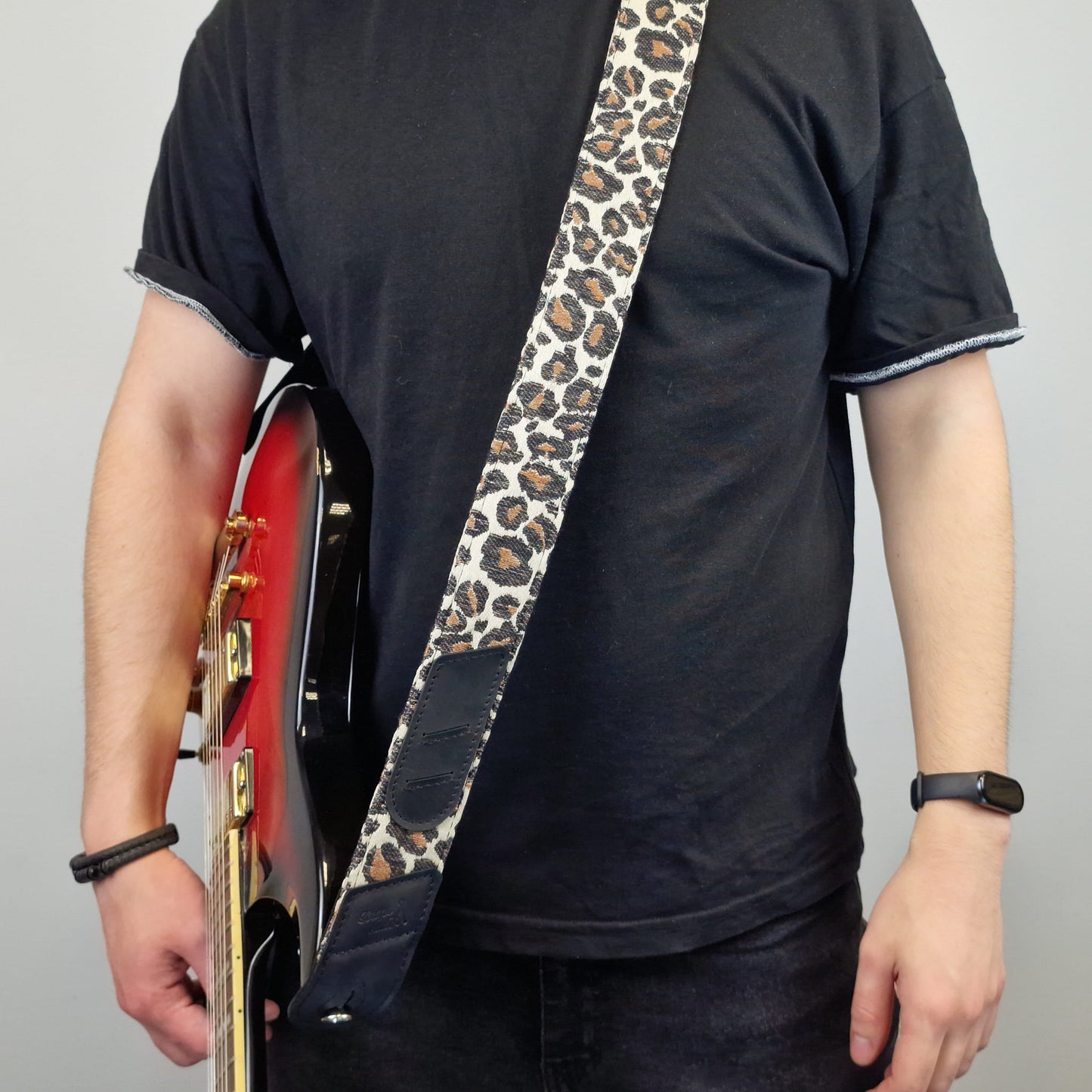leopard-print guitar strap with dark blue leather ends against a plain gray background.