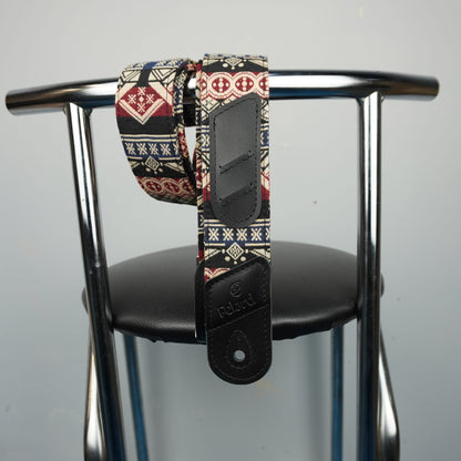 guitar strap with a colorful geometric pattern and black leather hardware, draped over the back of a black chair with a chrome frame.