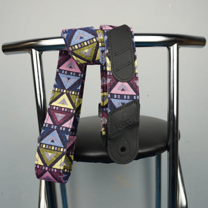Felard guitar strap with a colorful geometric pattern in pink, blue, yellow, and purple, draped over the back of a black chair with a chrome metal frame.