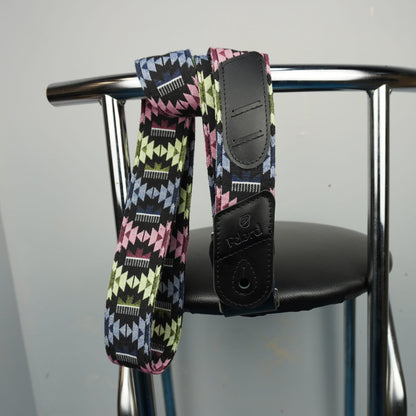 Felard guitar strap with a colorful geometric pattern and black leather ends, hanging from the back of a metal chair.
