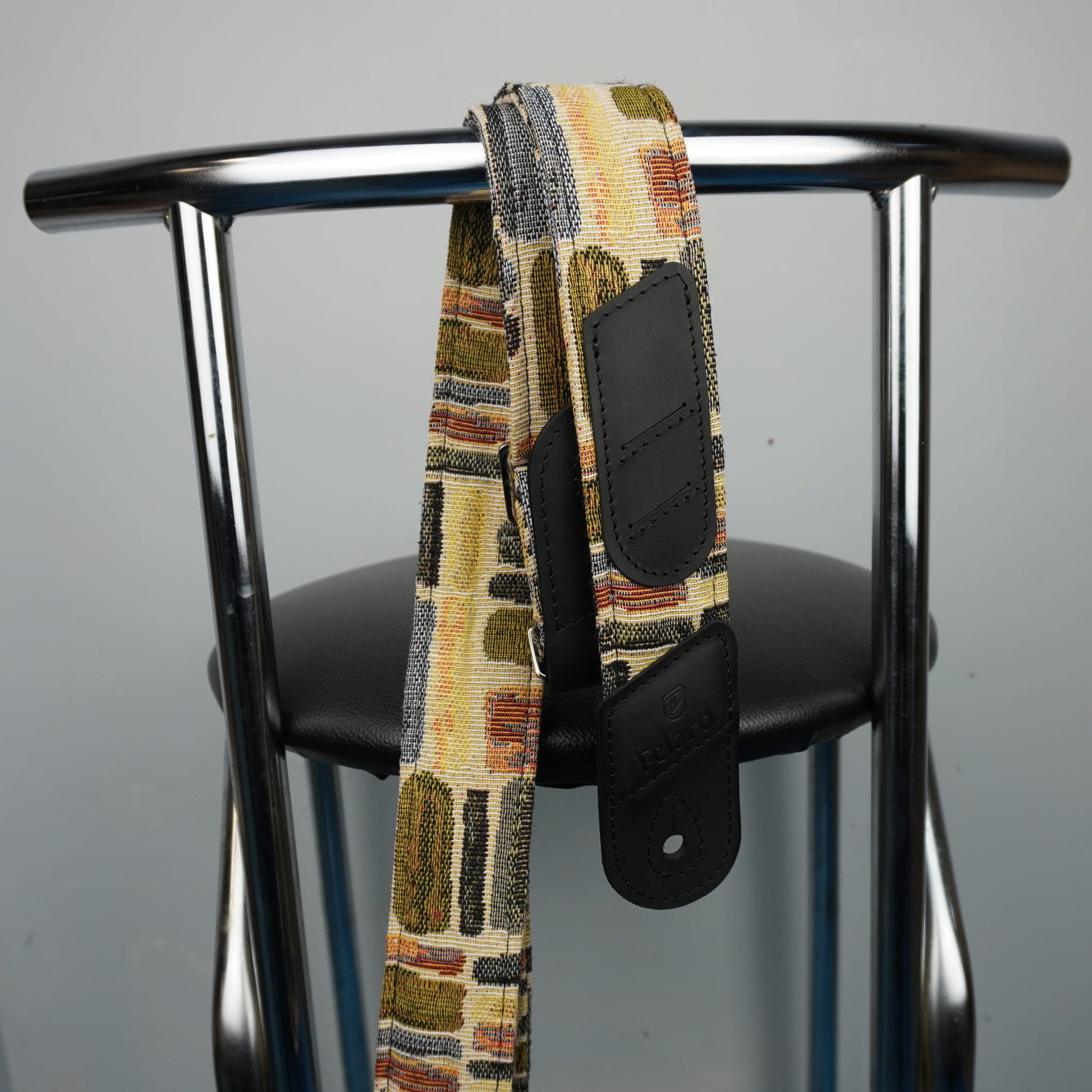 guitar strap with black leather hardware, draped over the back of a black chair with a chrome metal frame.