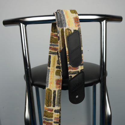 guitar strap with black leather hardware, draped over the back of a black chair with a chrome metal frame.