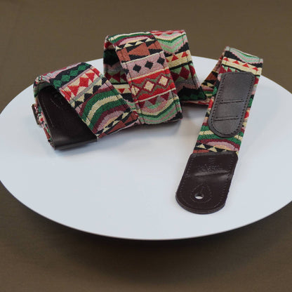 A guitar strap with a colorful geometric patterned fabric and dark brown leather ends, displayed on a white plate against a brown background.