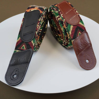 A pair of Felard guitar straps with a colorful geometric patterned fabric and brown leather ends, displayed on a white circular plate.