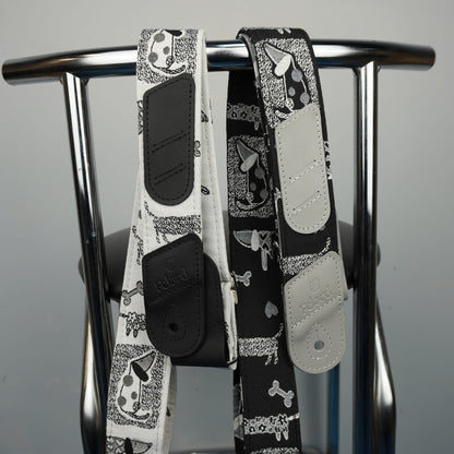 Two dog-print leather shoulder straps hanging from a metal stand against a plain light gray background.