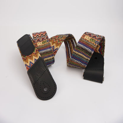 A multicolor woven guitar strap with black leather ends, displayed on a clean white background.
