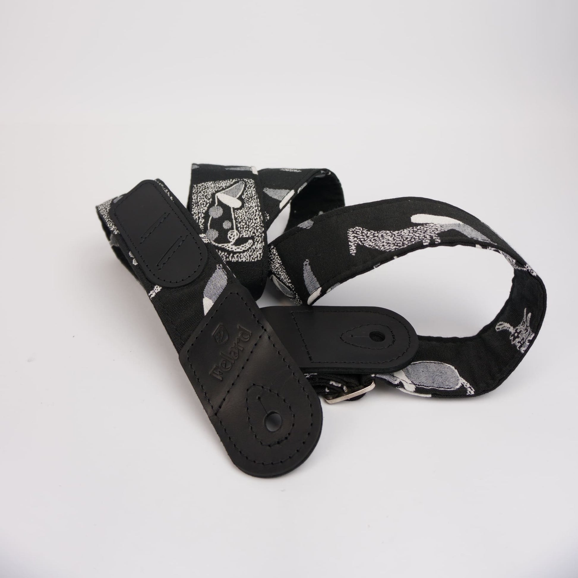 A black guitar strap featuring a gray and white abstract pattern, with a solid black leather keeper and metal buckle, displayed on a clean white background.