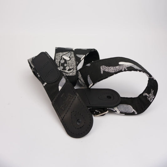 A black guitar strap featuring a gray and white abstract pattern, with a solid black leather keeper and metal buckle, displayed on a clean white background.