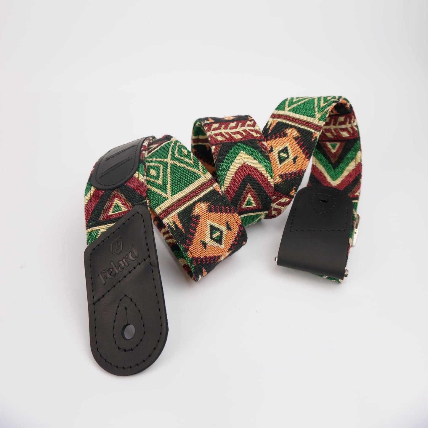 A giutar strap with a Southwestern geometric pattern in green, red, orange, and black, featuring black leather hardware.