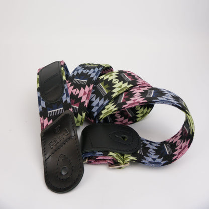 A multicolor geometric patterned guitar strap with black leather end caps, coiled on a white background.