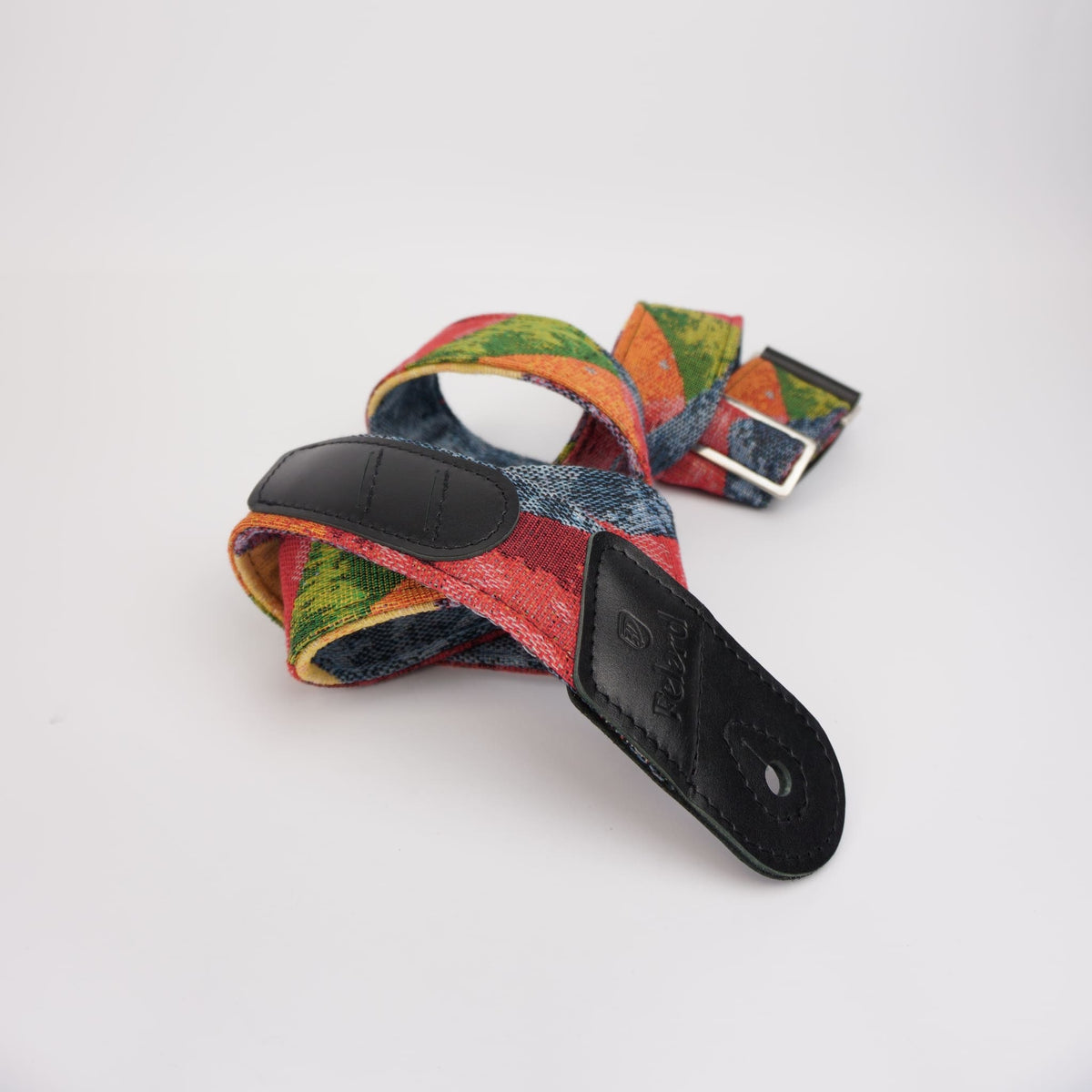 A colorful woven guitar strap with a multicolor pattern of red, green, orange, and blue, featuring black leather ends and a silver metal buckle, photographed on a white background.