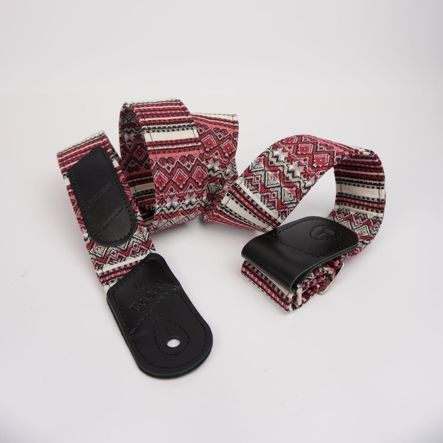 Guitar strap featuring a black leather ends and a woven fabric body with a red, black, and white geometric pattern, photographed on a white background.