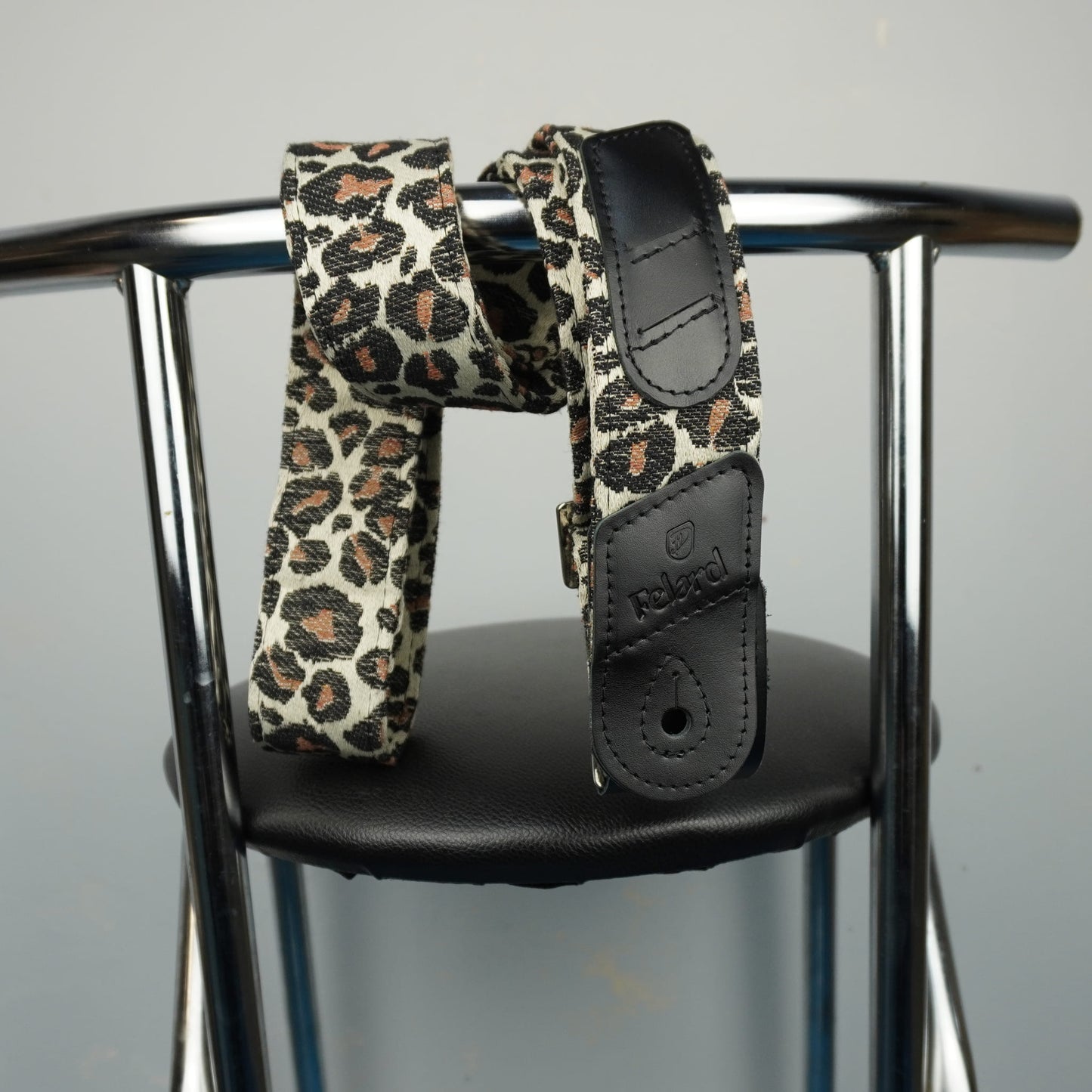 A leopard print waist strap with black faux leather accents, draped over the armrests of a chrome chair.
