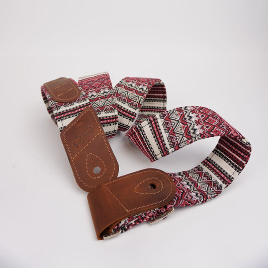 Guitar strap featuring a brown leather end piece and a woven fabric body with a red, black, and white geometric pattern, photographed on a white background.