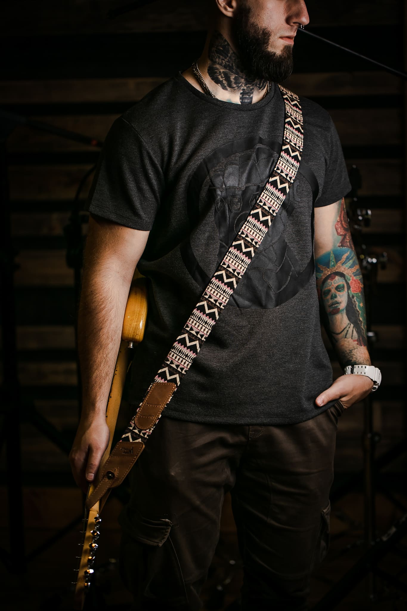 brown leather guitar strap with a cream geometric pattern. The background is a dark, dimly lit stage or studio environment.