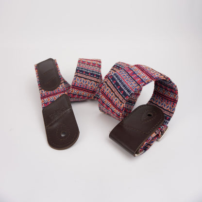 A guitar strap with a colorful geometric patterned fabric and dark brown leather ends, displayed on a clean white background.