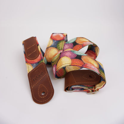 Guitar strap with a colorful fruit print and brown leather ends, shown on a plain white background.