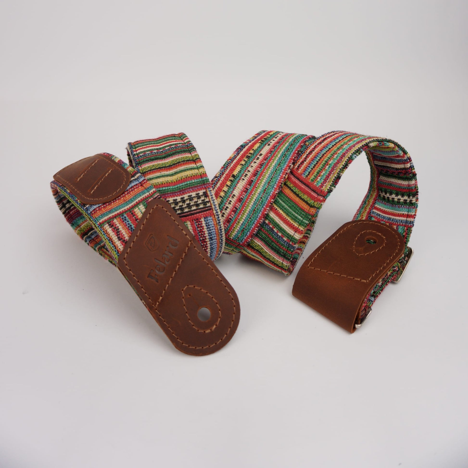 Guitar strap featuring a colorful woven textile with red, green, yellow, black, and white stripes, finished with brown leather ends and a metal snap button.