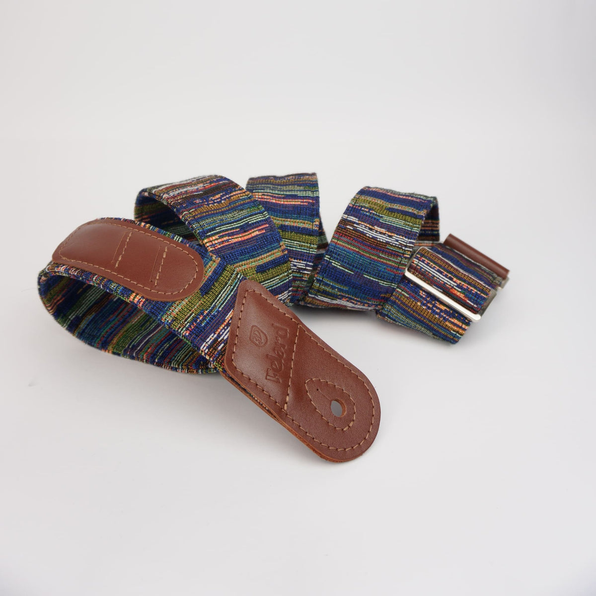 A multicolor woven guitar strap with brown leather end pieces, photographed on a clean white background.