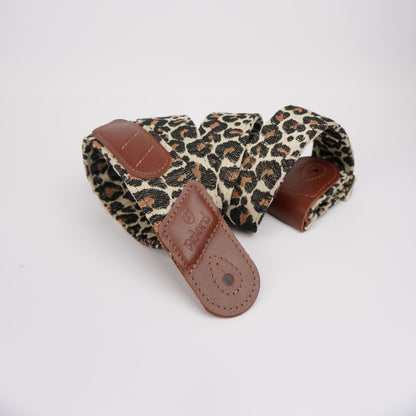 A leopard print guitar strap with brown leather accents, coiled on a plain white background