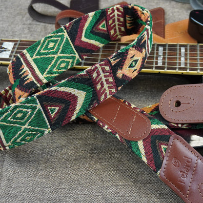 A close-up of a guitar strap with a colorful geometric pattern in green, red, beige, and black, featuring brown leather end pieces and a visible 'Iceland' brand patch.