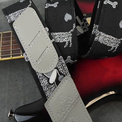 guitar strap with a black background, white and gray dog pattern, and light gray adjustable padded sections. The strap is draped over a red and black electric guitar.