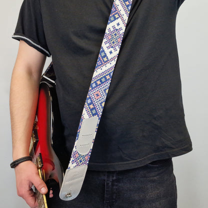 showcasing a patterned guitar strap with blue, white, and red geometric designs and silver metal hardware.
