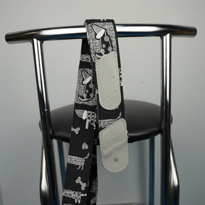 A black guitar strap with a white and gray dog bandana print and light gray adjustable plastic sliders, draped over the back of a chrome metal chair.