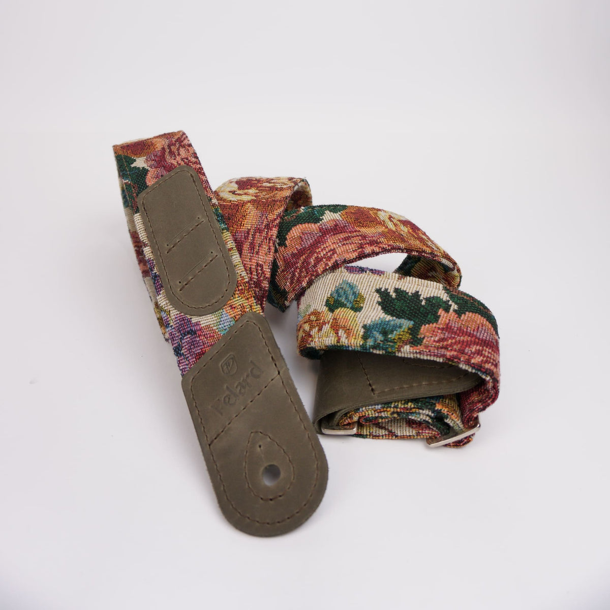 A guitar strap with a dense floral tapestry pattern in red, green, and orange, featuring olive brown leather end caps and a matching stitched loop, displayed on a clean white background.