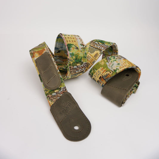 A guitar strap featuring a detailed vintage cityscape print in muted green, yellow, and brown tones, with olive green leather end-caps and loops.