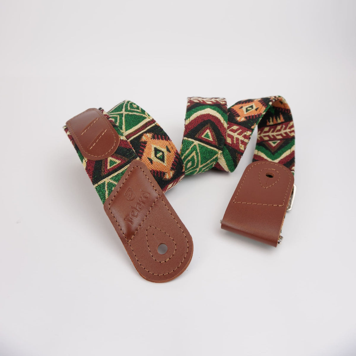 A guitar strap with a brown leather end pieces and a woven fabric body featuring a Southwestern geometric pattern in green, red, orange, and black, displayed on a clean white background.