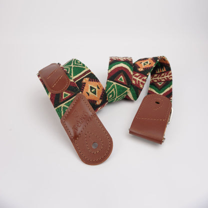 A guitar strap with a brown leather end pieces and a woven fabric body featuring a Southwestern geometric pattern in green, red, orange, and black, displayed on a clean white background.
