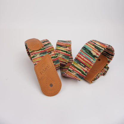 Colorful striped guitar strap with tan leather ends, one of which is embossed with the brand name 'Rolan'.