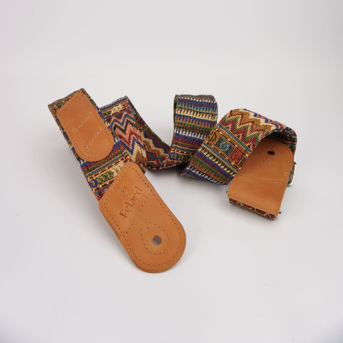A Felard guitar strap with a multicolor geometric patterned fabric and tan leather ends, displayed on a clean white background.