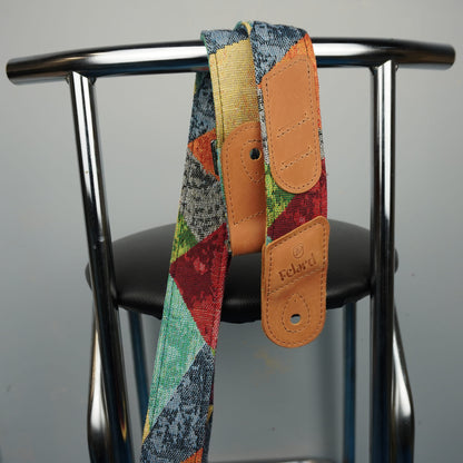 A colorful patchwork-patterned camera strap with tan leather accents hanging from a black chair against a gray background. The strap features the 'Focalland' brand name embossed on the leather tabs.