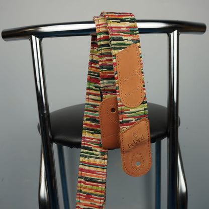 Guitar strap with a multicolor striped fabric and tan leather patches, hanging from the backrest of a metal chair.