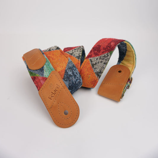 Guitar strap featuring a vibrant multicolor patchwork textile pattern with tan leather end-caps, displayed on a clean white background.