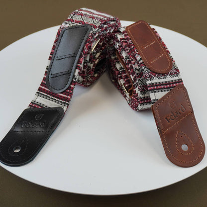 Guitar strap with a multicolor geometric patterned fabric body, brown leather end caps, and black leather hardware, displayed on a white circular plate.