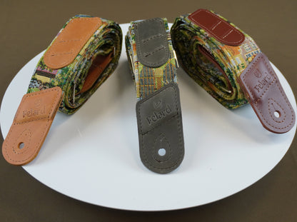 Three Focal brand guitar strap adjusters or strap components displayed on a white circular plate against a dark brown background. The center item is a dark gray metal piece with a green and yellow plaid fabric strap, while the side items show camouflage and brown leather patterned straps.