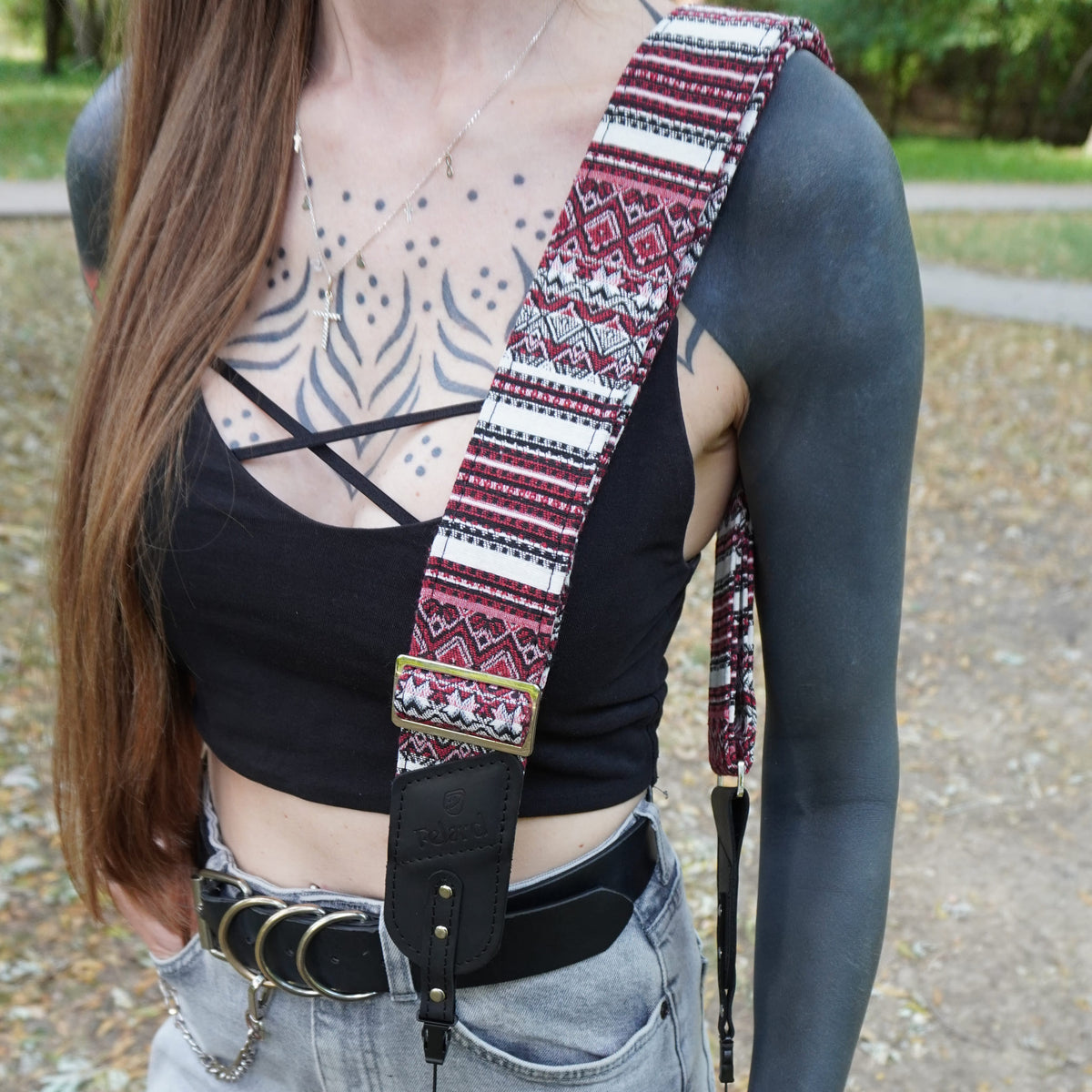 A person outdoors holding leather camera strap with a patterned tapestry fabric core. 