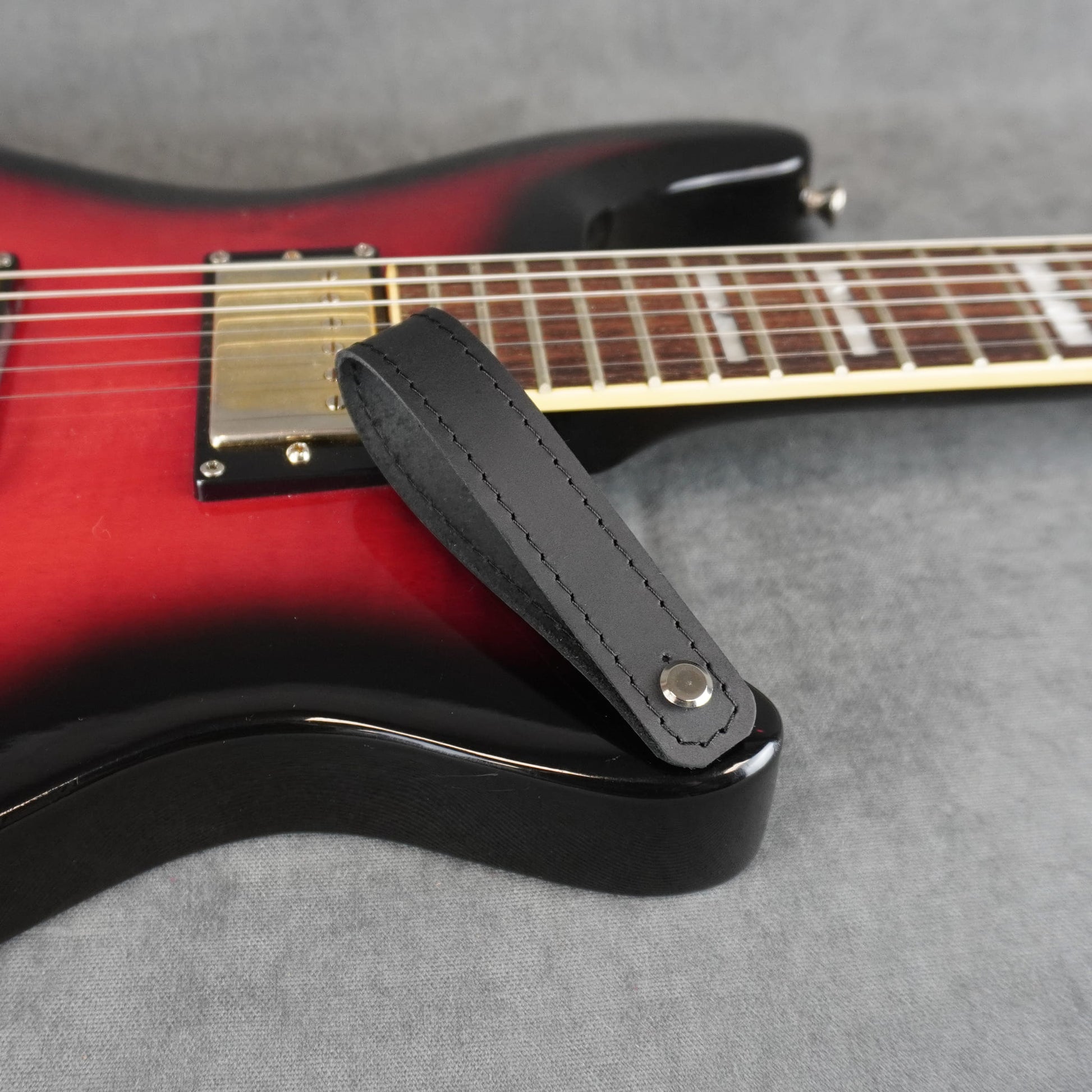A close-up of an electric guitar with a black matte leather guitar headstock adapter